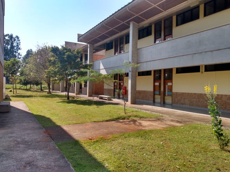Em primeiro plano um gramado com algumas árvores de altura média e no segundo plano, no térreo, as salas de docentes do DGTH e no piso superior salas do DCHE.